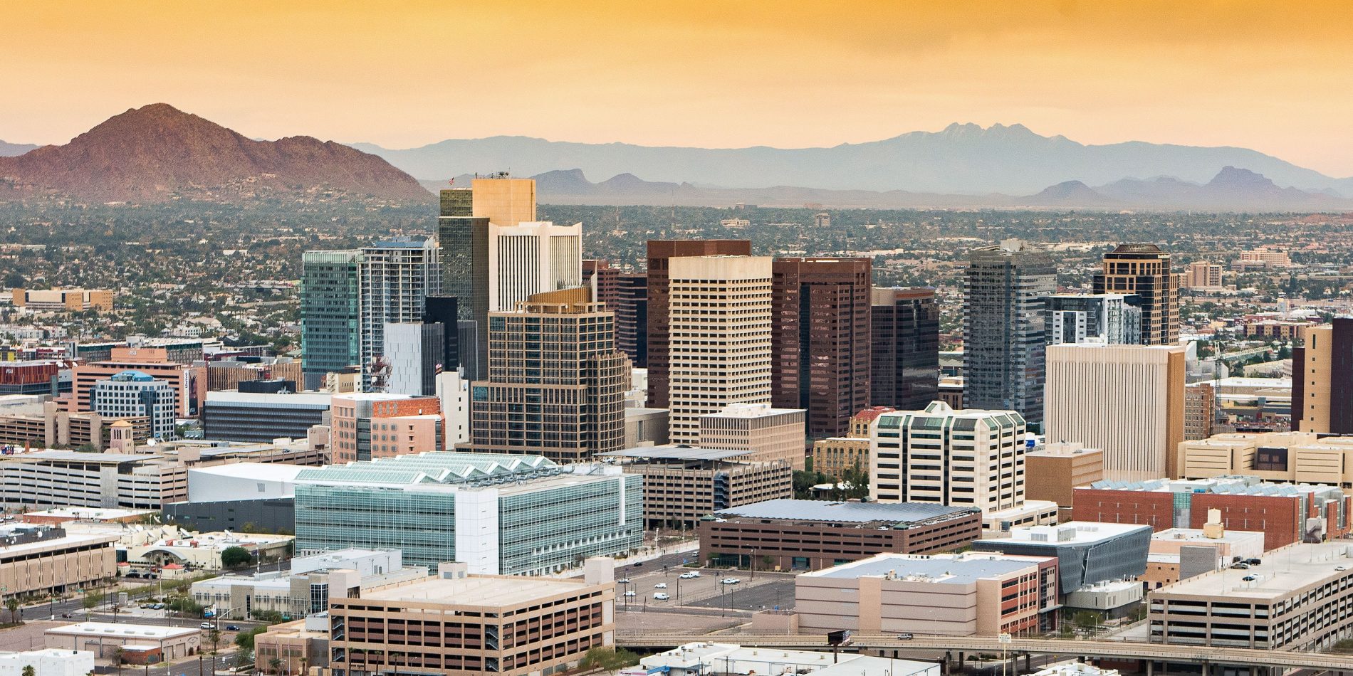 City scape of Phoenix at sunset with skyscapers in the foreground and mountains in the background