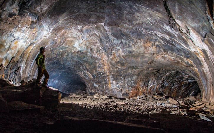 A man stands in shadow, a light illuminating a cave system with two tunnels