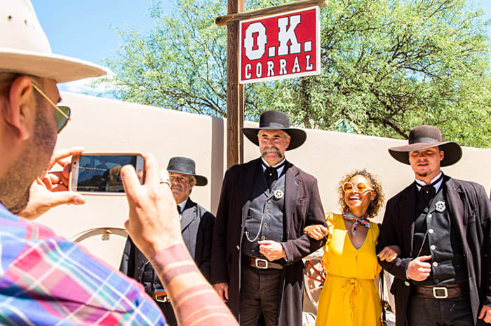 A woman in a yellow dress smiles as she poses with male actors in Old West costumes