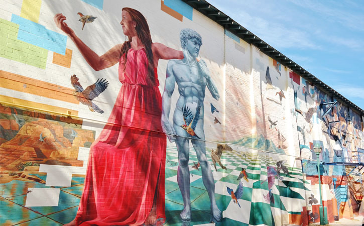 A large mural spans the length of a building's exterior wall. The image is a contemporary depiction of sound and performance.