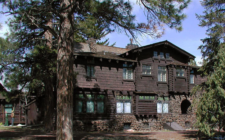 An Arts & Craft-style two-story mansion sits among a forest of pine trees.
